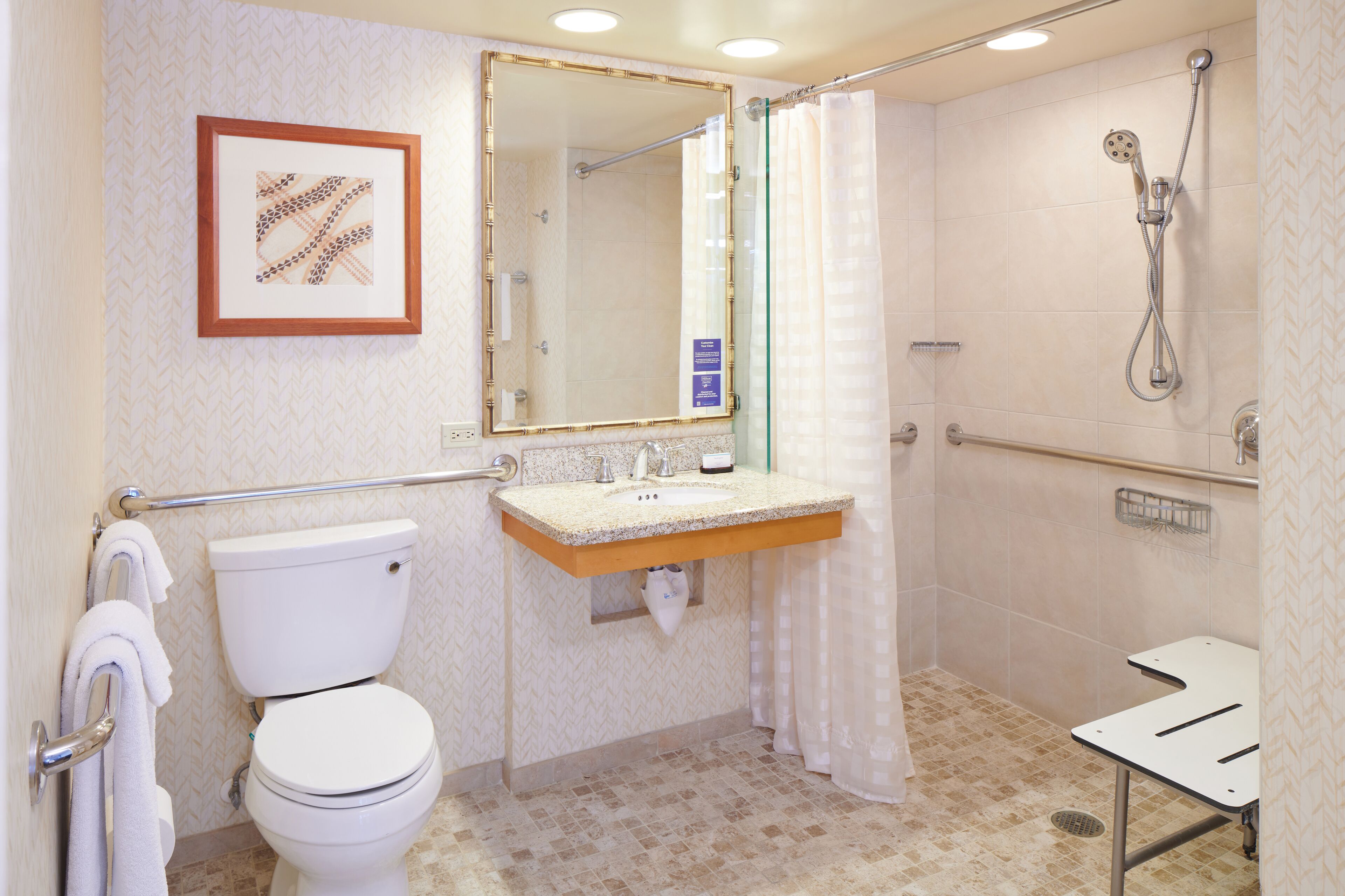 A bathroom with a toilet, sink, shower, and a framed picture on the wall.