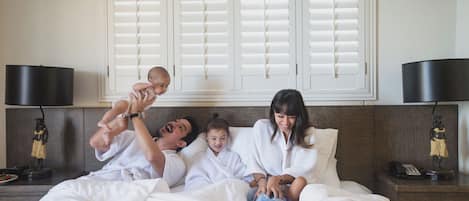 A family of four in a hotel room with a bed, nightstands, and a window with shutters.
