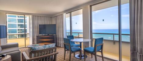 Habitación de hotel con balcón, televisión, sofá, mesa de centro y vista al océano.