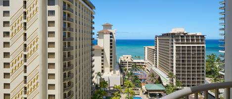 A high-rise hotel with multiple floors, a pool area with palm trees, and a view of the ocean.