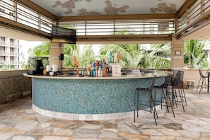 A bar area with a tiled pool, bar stools, and a television mounted on the wall.