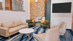Un salon moderne avec un canapé beige, deux fauteuils, une table basse et un mur en pierre sur lequel est fixé un téléviseur.