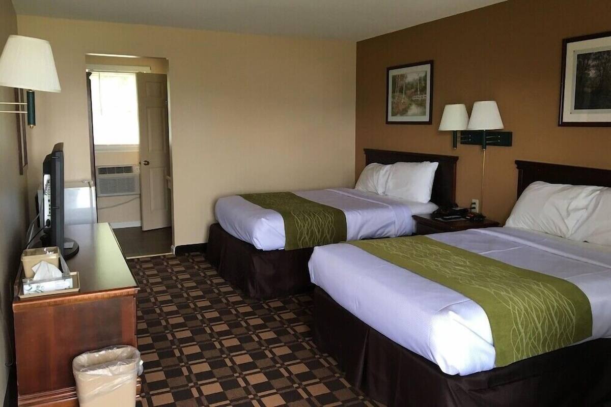 A hotel room with two beds, a desk with a computer, a trash bin, and a door leading to a bathroom.