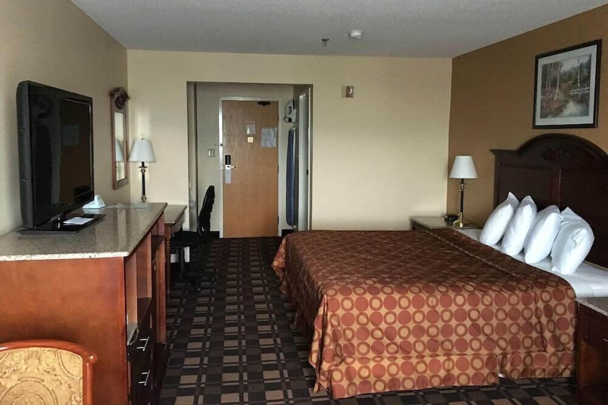 A hotel room with a bed, a desk, a chair, a TV, and a door leading to another room.