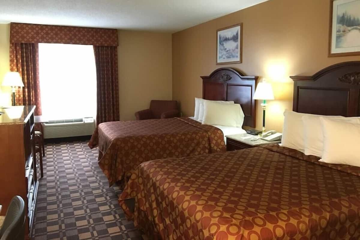 A hotel room with two beds, a desk, a chair, a window with curtains, and a painting on the wall.