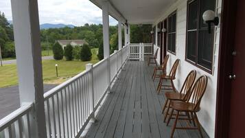 Une véranda avec des chaises en bois et une balustrade blanche.
