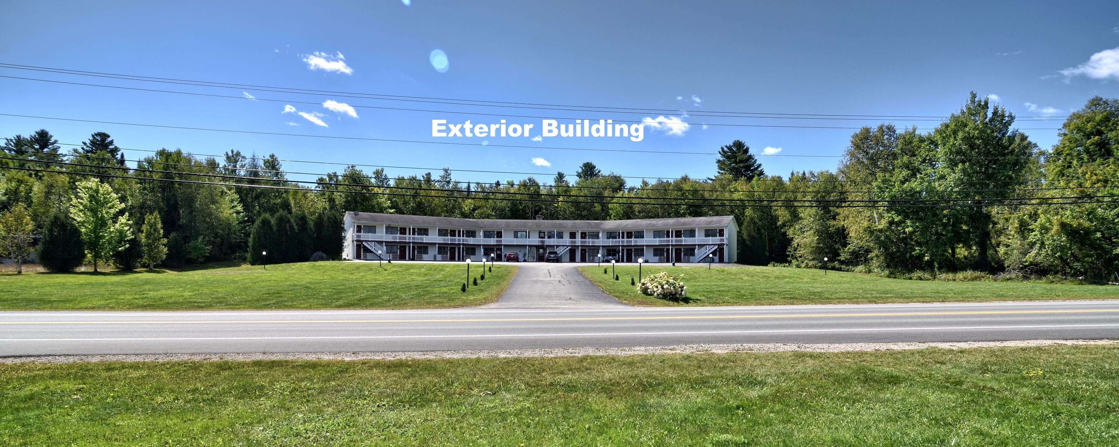 Edificio de dos pisos con entrada central, rodeado de un césped cuidado y árboles.