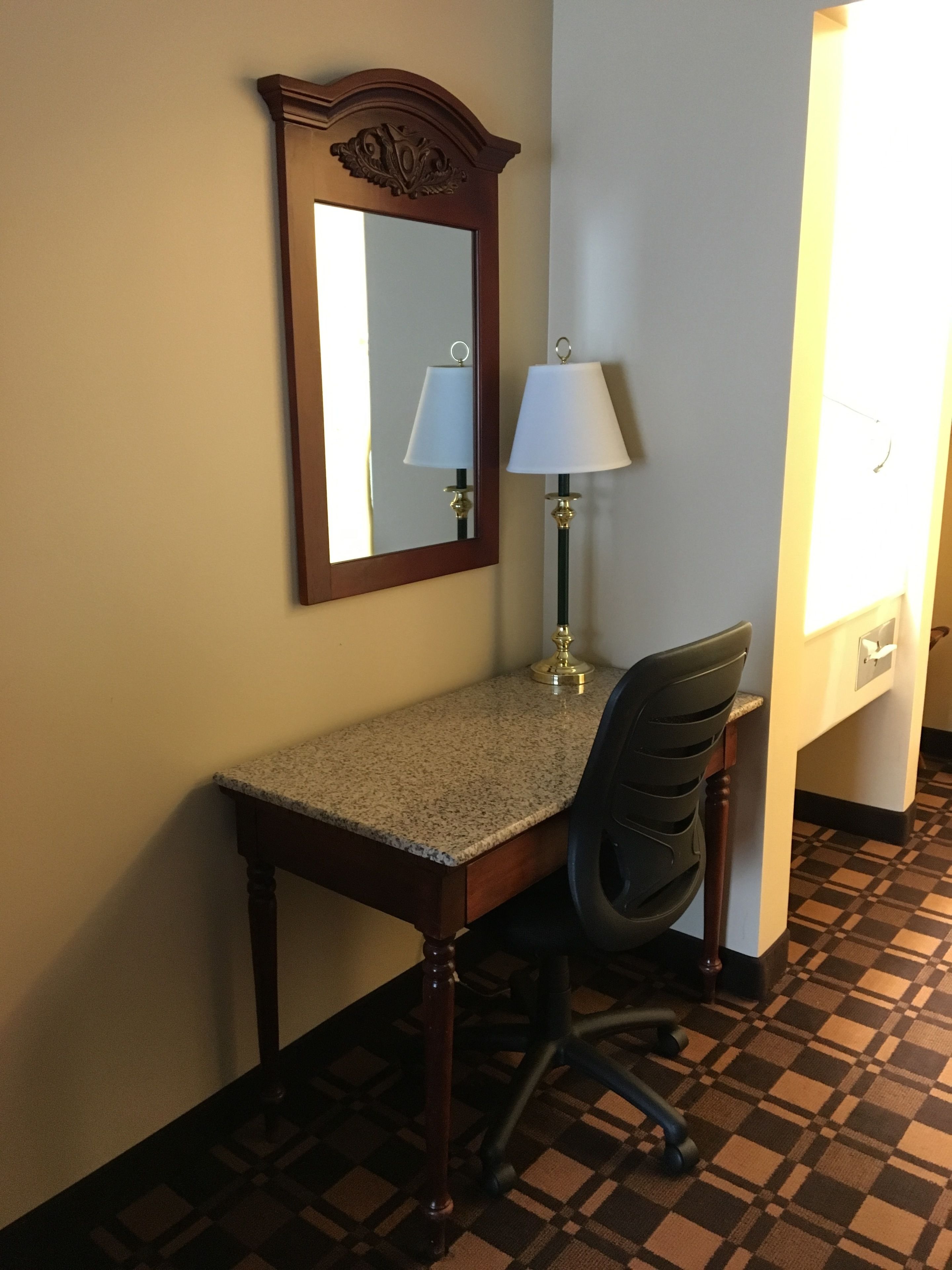 A small desk with a chair, a lamp, and a mirror in a hotel room.