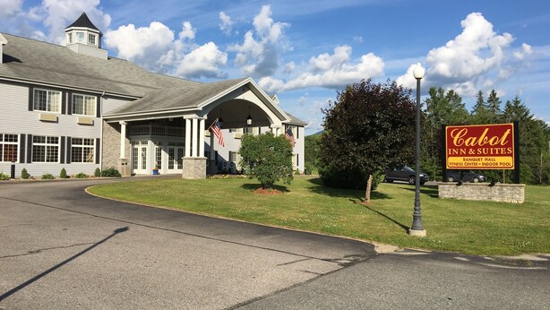 A hotel with a large sign for Cabot Inn & Suites, featuring amenities like a banquet hall, fitness center, and indoor pool.