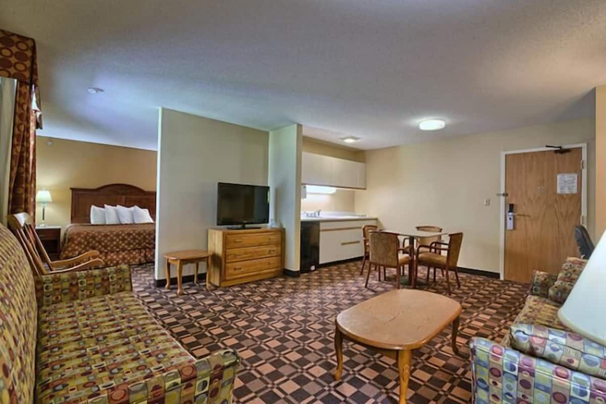 A hotel room with a bed, a TV, a small table, a sofa, and a kitchenette.