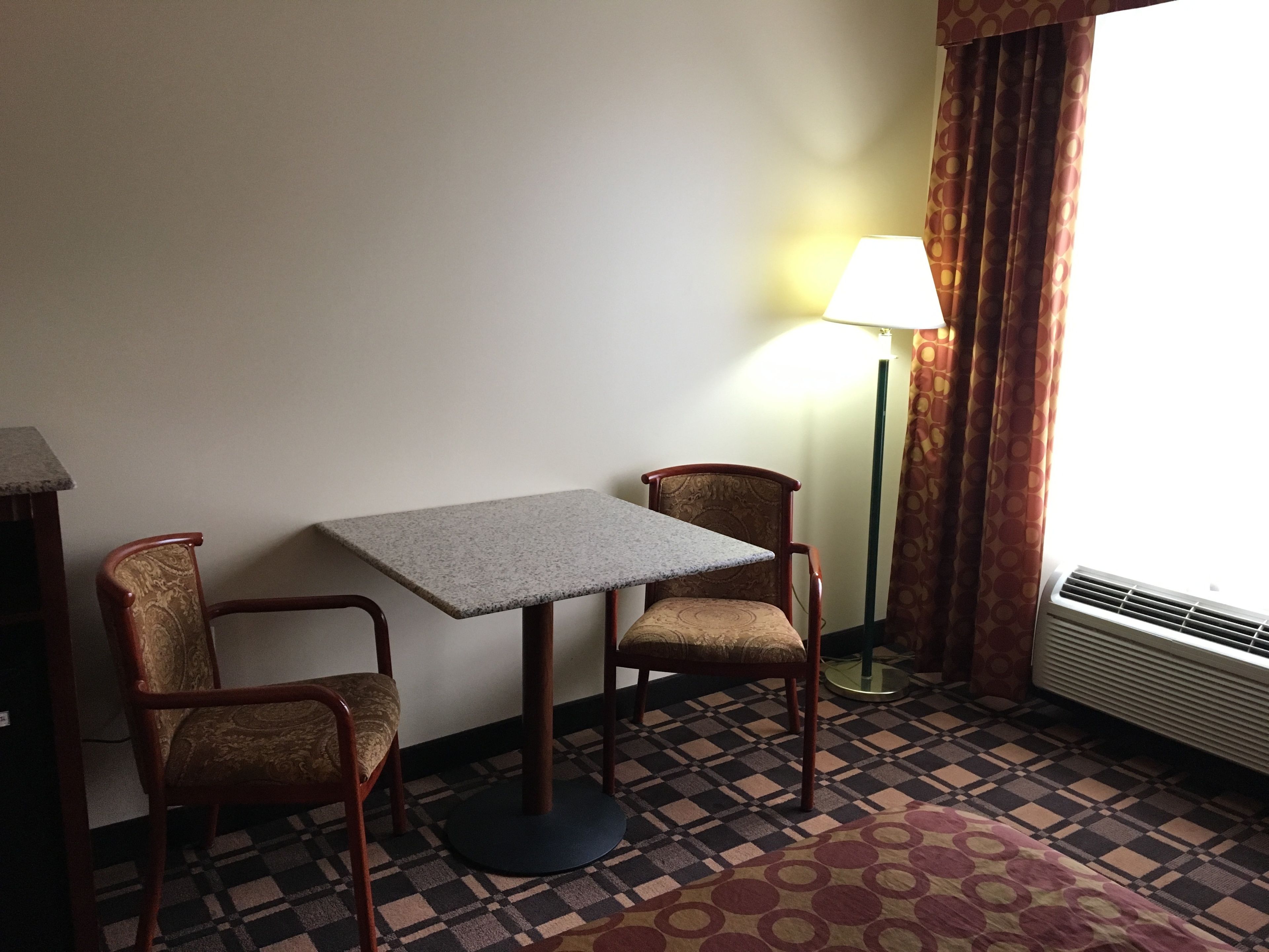 A small room with a table and two chairs, a lamp, and a window with curtains.