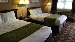 A hotel room with two beds, a desk, and a chair. There are two lamps on the desk and a window with curtains.