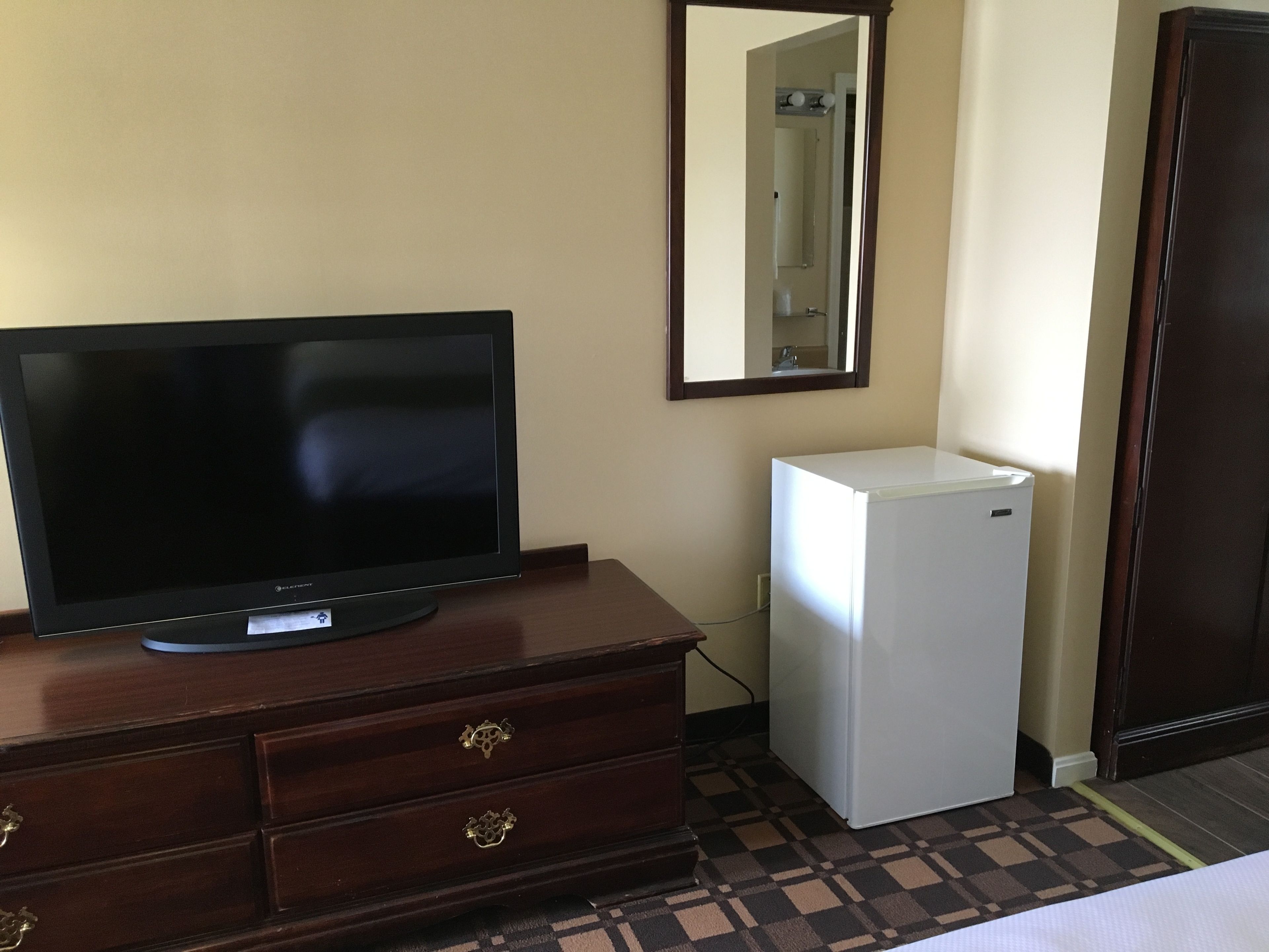Una habitación con una televisión sobre un tocador de madera, un refrigerador blanco pequeño y un espejo en la pared.