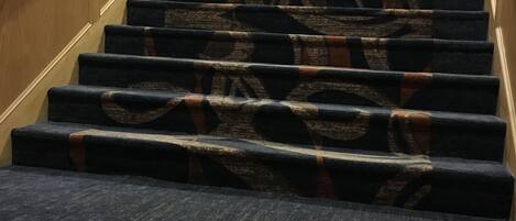 A carpeted staircase with a wooden handrail and a patterned carpet.