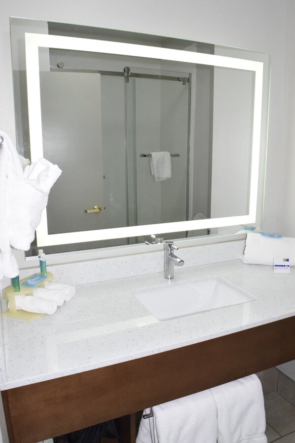 A bathroom with a large mirror, a sink, and a shower visible in the reflection.