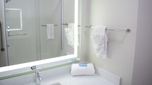 A bathroom with a large mirror, a glass shower enclosure, a towel rack, and a sink with a white countertop.