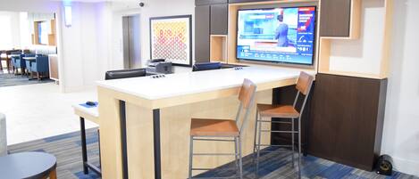 A modern hotel lobby with a reception desk, seating area, and a television displaying a weather forecast.