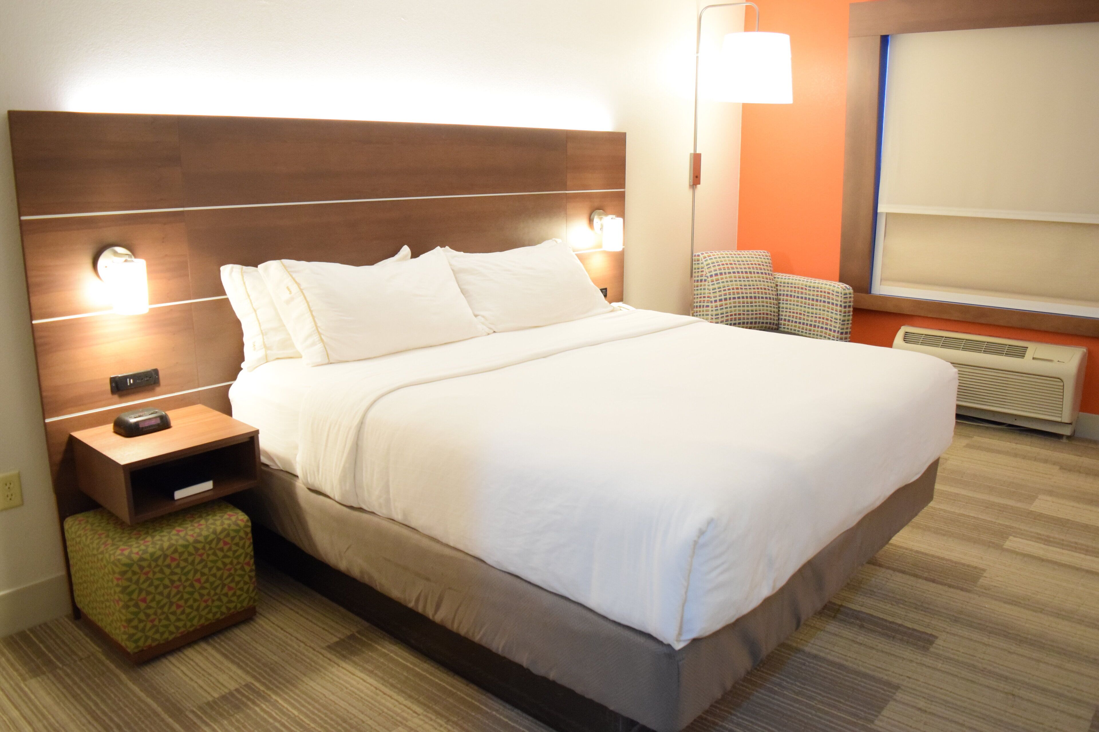 Een hotelkamer met een groot bed, een nachtkastje, een stoel en een raam met jaloezieën.