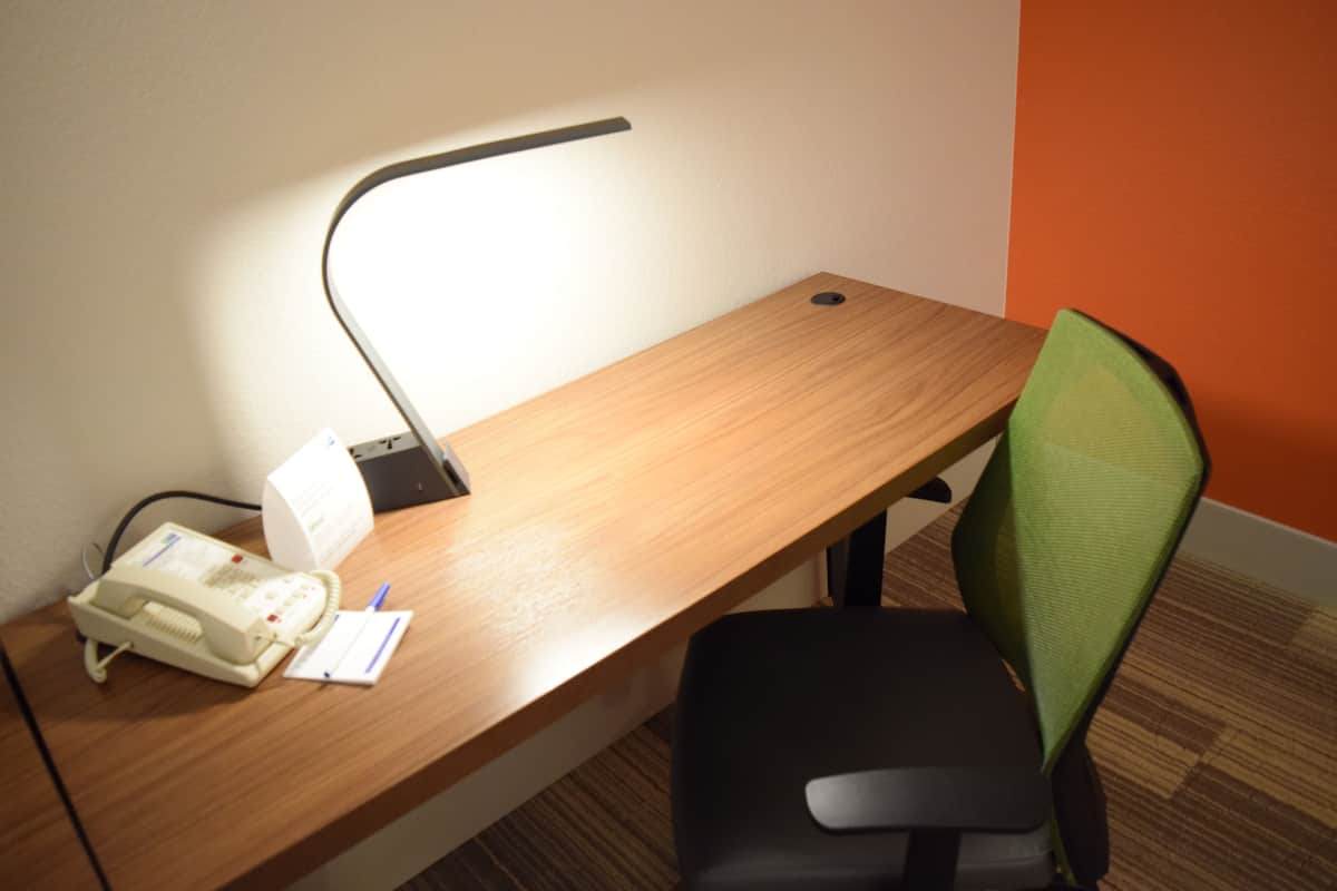 Un escritorio de madera con un teléfono, una lámpara y una silla verde.