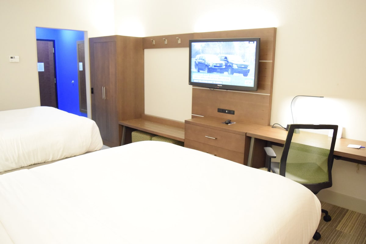 Habitación de hotel con dos camas, un escritorio con computadora, televisión y una silla.