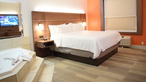 A hotel room with a large bed, a TV on the left, a bathroom with a bathtub, and a window with blinds.
