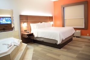 Habitación de hotel con una cama grande, un televisor a la izquierda, un baño con bañera y una ventana con persianas.