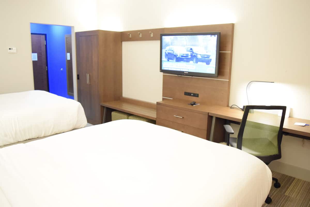 Habitación de hotel con dos camas, un escritorio con computadora, televisión y una silla.