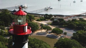 A lighthouse with a black and white striped tower, a red roof, and a white building with a red roof nearby.