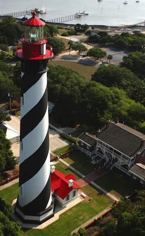 Un faro con una torre a rayas blancas y negras, un techo rojo, y un edificio cercano con techo rojo.