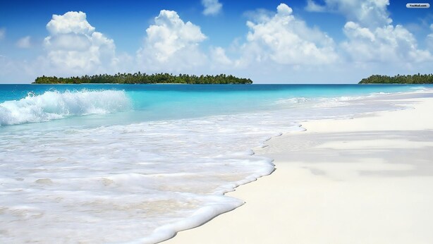 A beach with clear turquoise water, white sand, and a small island with trees in the background.