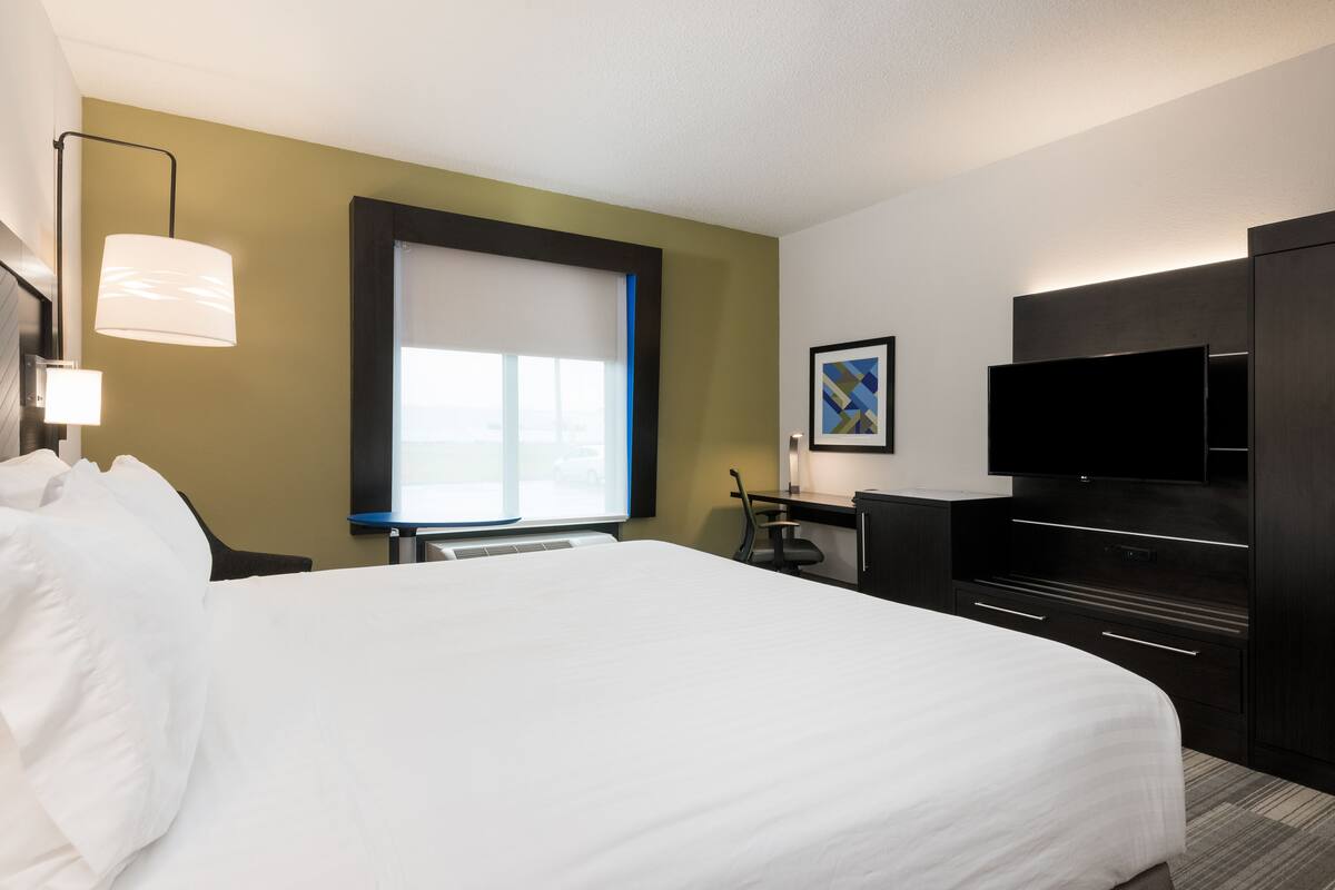 Habitación de hotel con una cama grande, un escritorio con silla, un televisor de pantalla plana y una ventana con persianas.