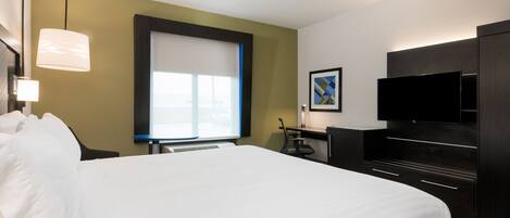 A hotel room with a large bed, a desk with a chair, a flat-screen TV, and a window with blinds.