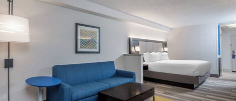 Habitación de hotel con cama, sofá azul, una mesita, lámpara y un cuadro en la pared.