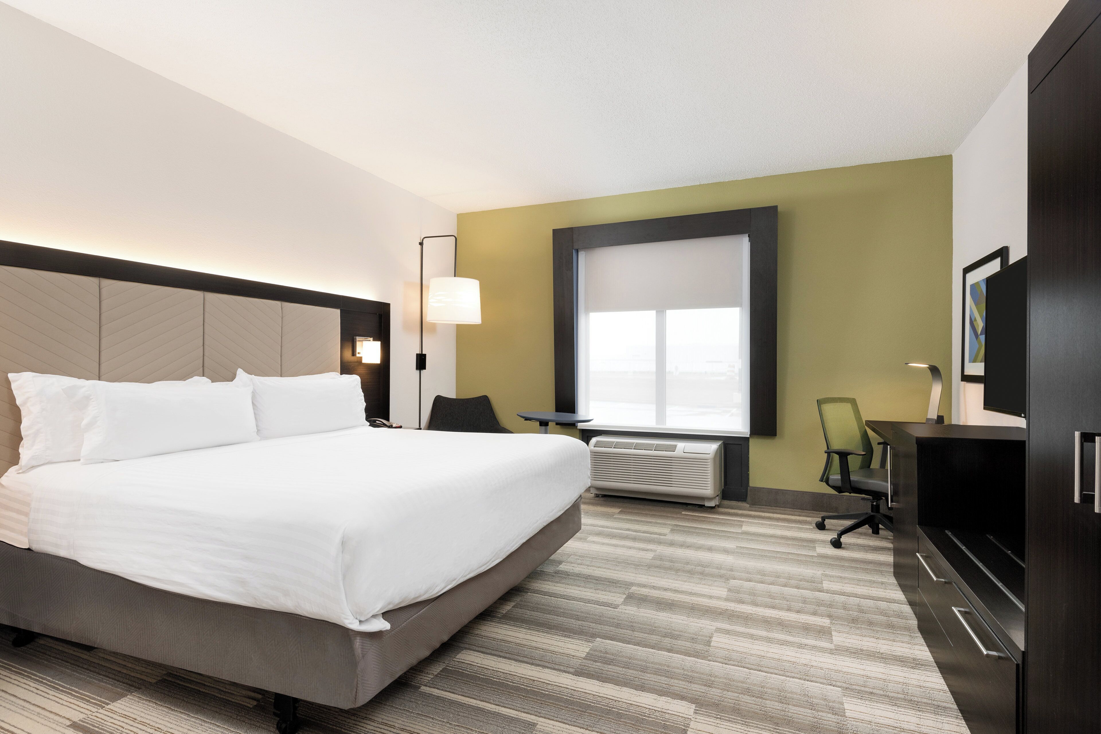 A hotel room with a large bed, a desk, a chair, a TV, and a window.