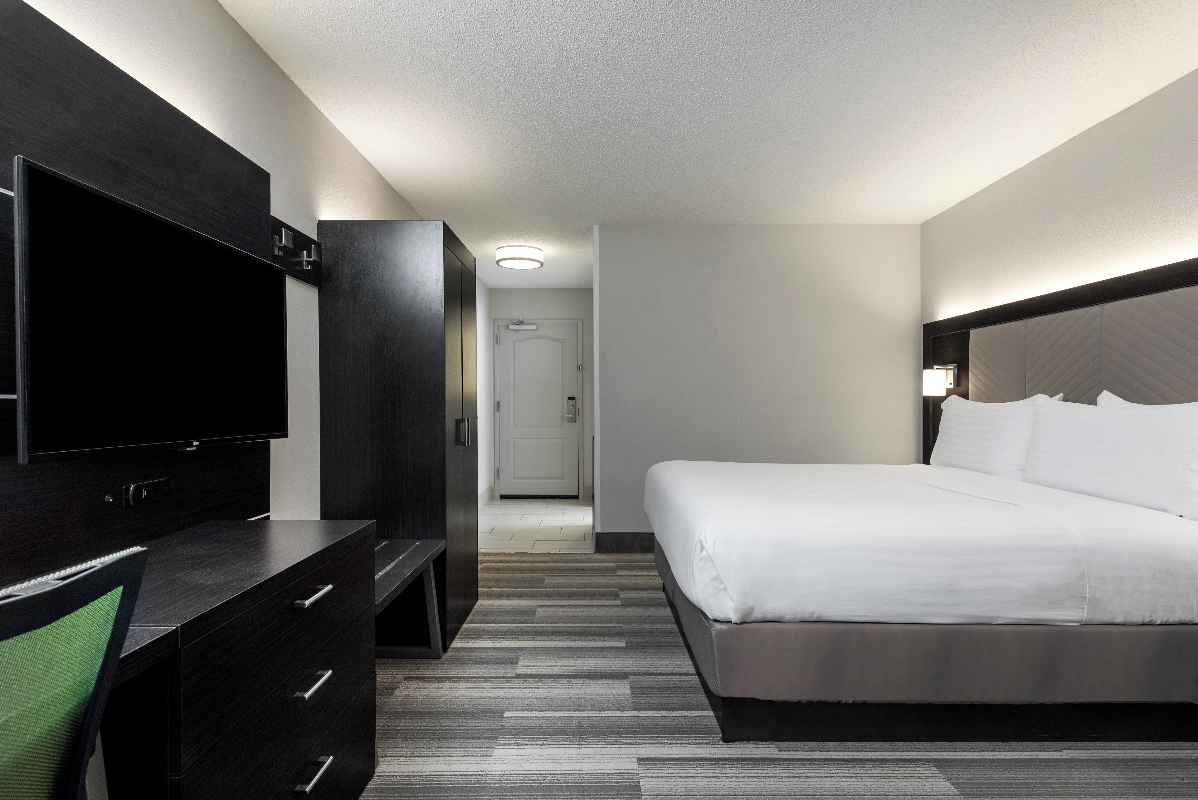 A hotel room with a bed, a TV, a dresser, and a door leading to a hallway.