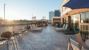 Un patio al aire libre con sillones y mesas, un edificio de ladrillo y cielo despejado.