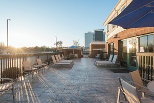 Un patio al aire libre con sillones y mesas, un edificio de ladrillo y cielo despejado.