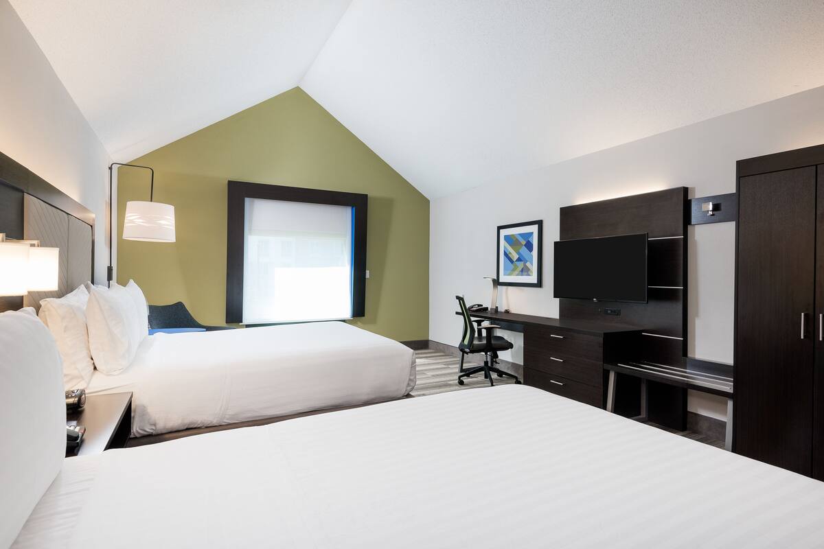 Una habitación de hotel con dos camas, un escritorio, una silla, un televisor y un ventanal grande.