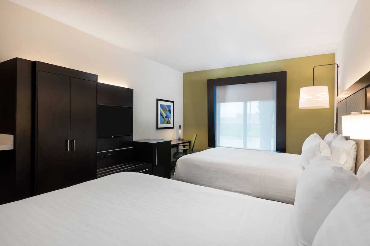Habitación de hotel con dos camas, un escritorio, un televisor y una ventana con vistas.