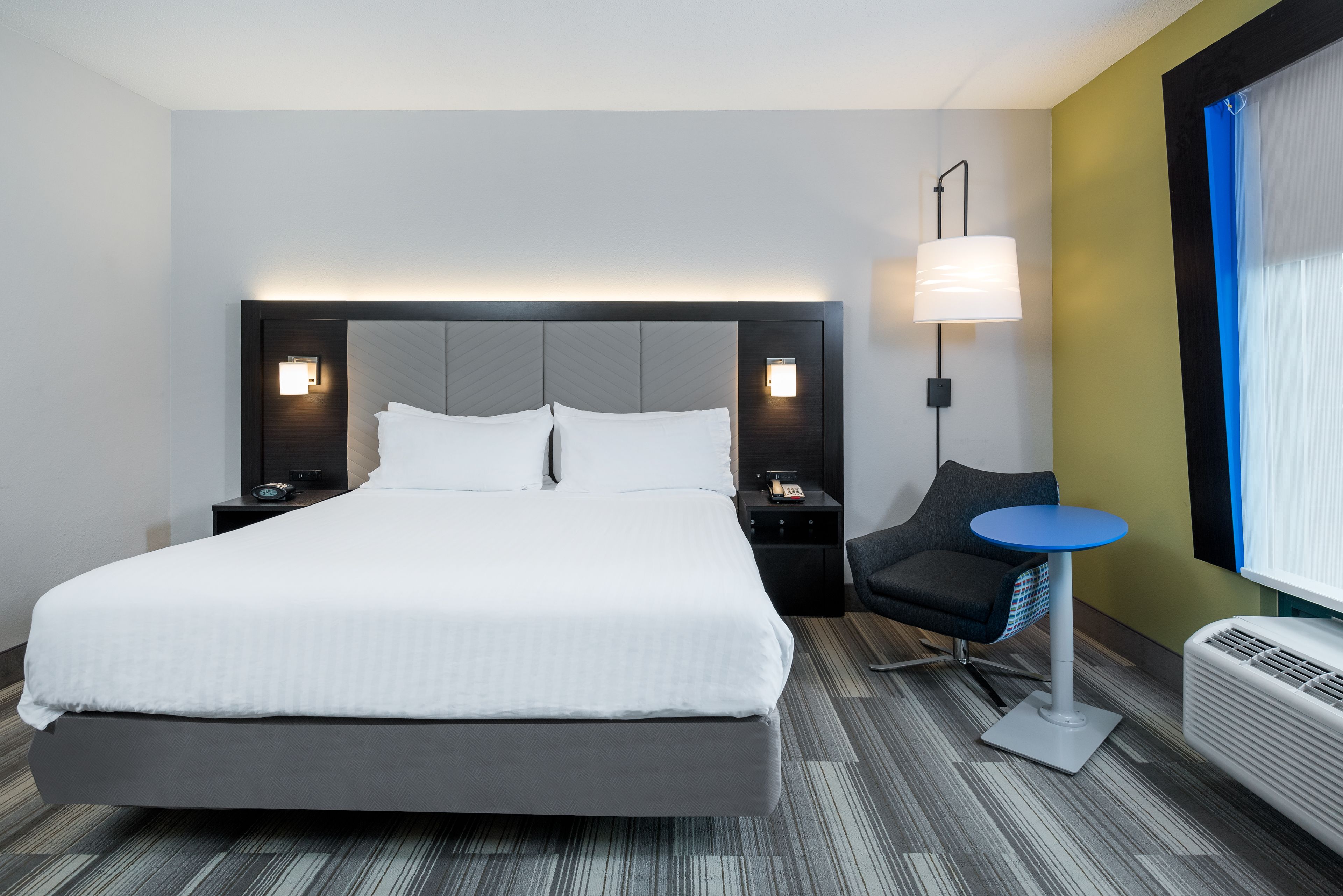 Una camera d'albergo moderna con un letto grande, lampade sui comodini, un tavolino, una sedia e una finestra con persiane.