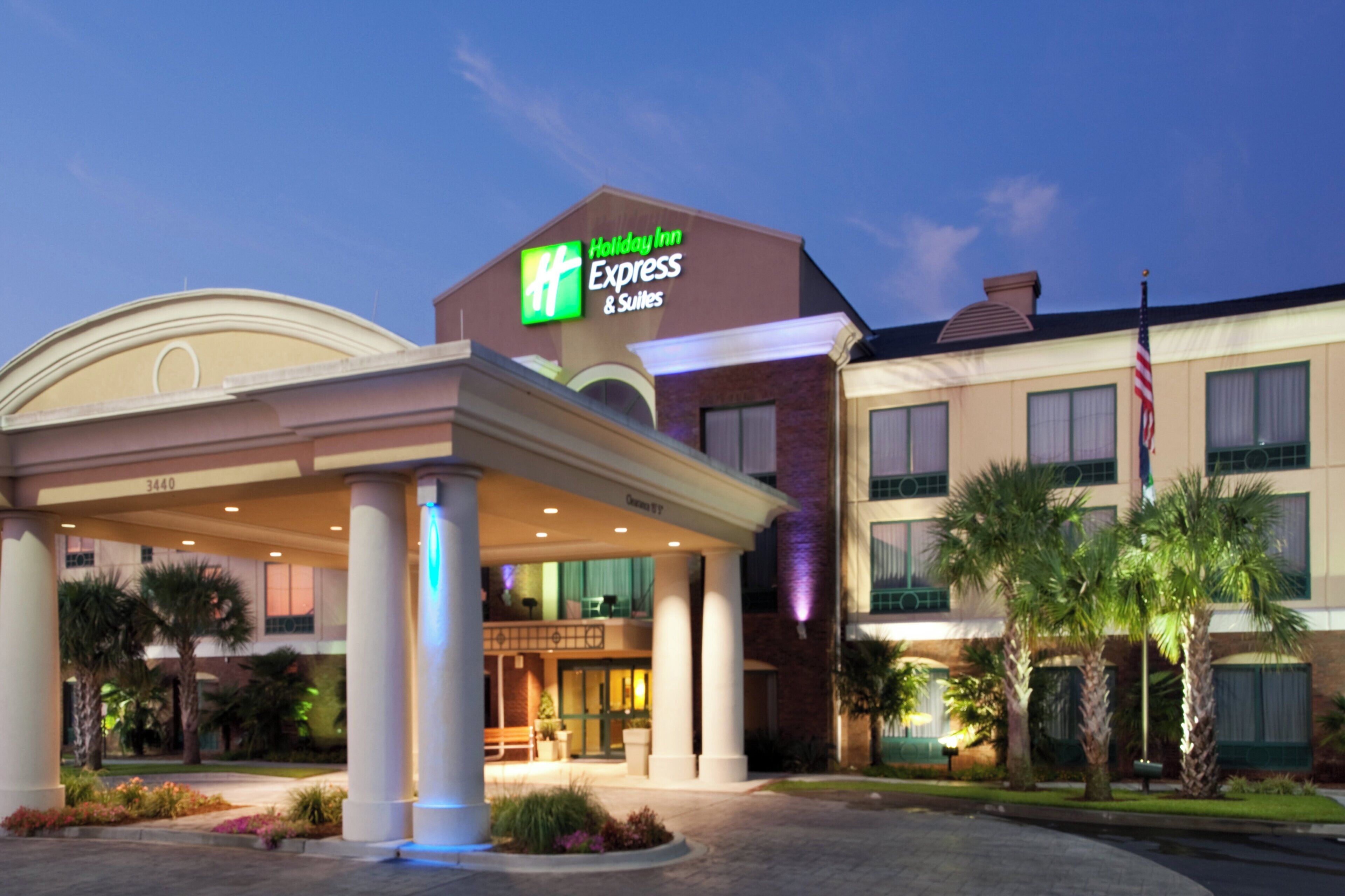 Un hotel Holiday Inn Express & Suites con entrada techada, palmeras y una bandera estadounidense.