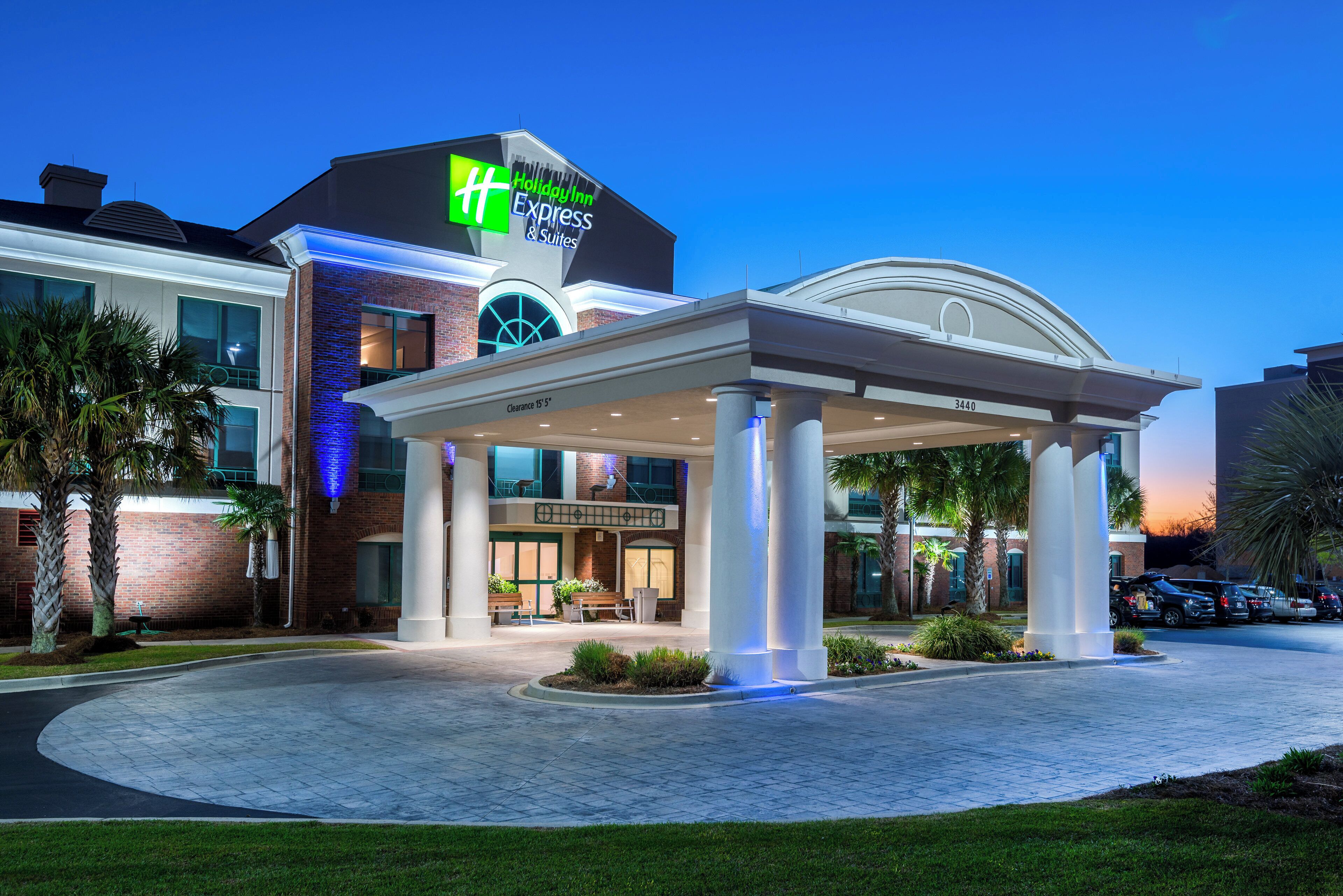 A Holiday Inn Express & Suites hotel with a covered entrance, palm trees, and a clear sky.