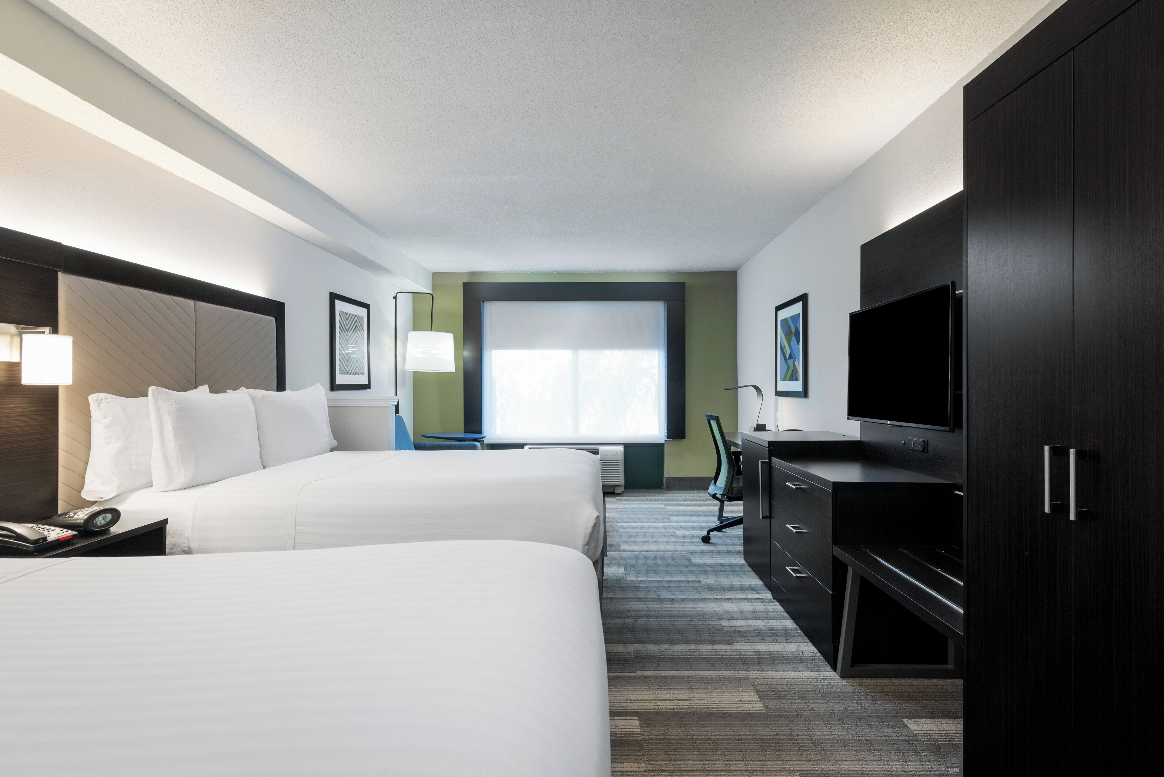A hotel room with two beds, a desk, a chair, a television, and a large window.