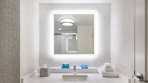 Une salle de bain moderne avec un grand miroir, un lavabo blanc et des articles de toilette.