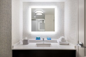 Une salle de bain moderne avec un grand miroir, un lavabo blanc et des articles de toilette.