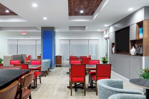 Una sala de conferencias moderna con mobiliario rojo y gris, un pilar azul y un televisor montado en la pared.