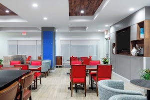Una sala de conferencias moderna con mobiliario rojo y gris, un pilar azul y un televisor montado en la pared.