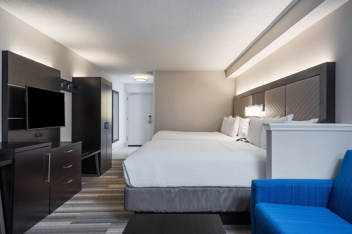 Habitación de hotel con una cama, televisión, escritorio y una silla azul.