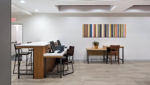 Un espacio de oficina moderno con una mesa larga, dos sillas, un escritorio con una computadora y una obra de arte colorida colgada en la pared.