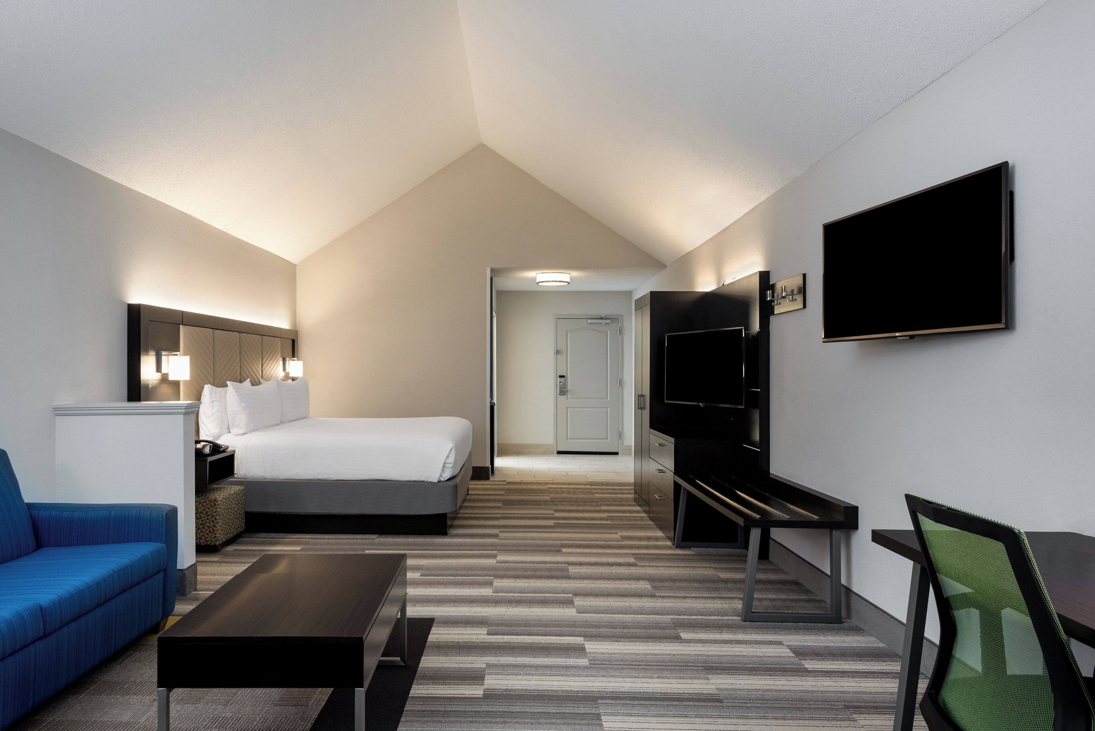 Una habitación de hotel con cama, escritorio, silla, televisor y sofá.